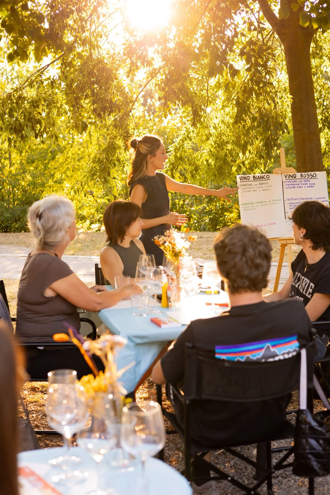 Laboratorio creativo all'aperto, con persone sedute in ascolto sotto gli alberi